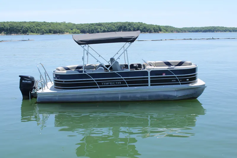 The Image of 2022 Trifecta RFLE pontoon boat with Suzuki motor on a calm lake. - 1