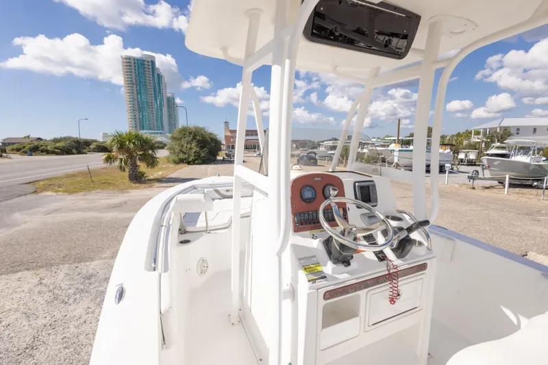 Slide: The Image of 2012 Sea Hunt Ultra 225 boat interior with steering wheel, parked near a coastal road. - 22
