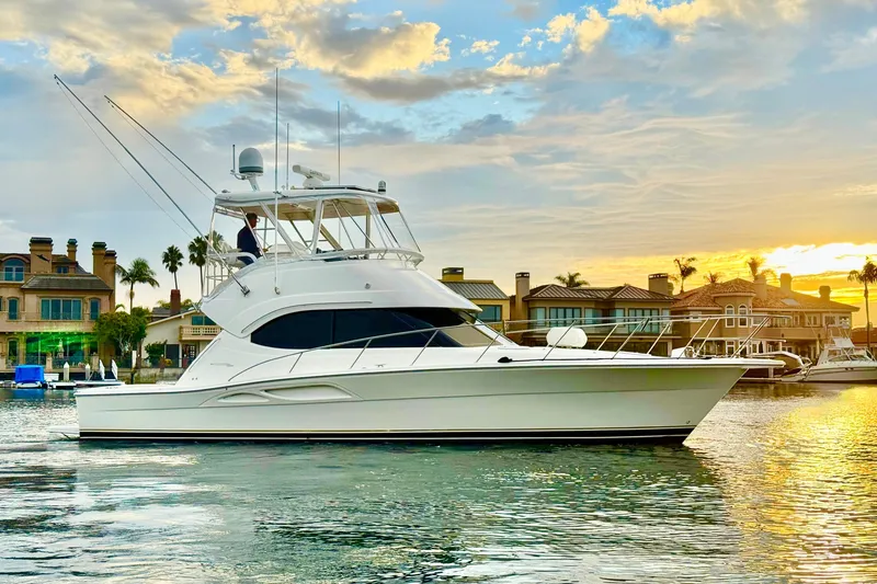The Image of 2001 Riviera 40 Flybridge yacht cruising at sunset near waterfront homes. - 0