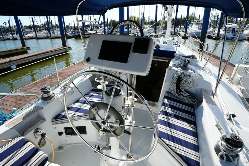 Slide: The Image of 1983 Hunter 34 sailboat cockpit with striped seating, steering wheel, and marina view. - 10