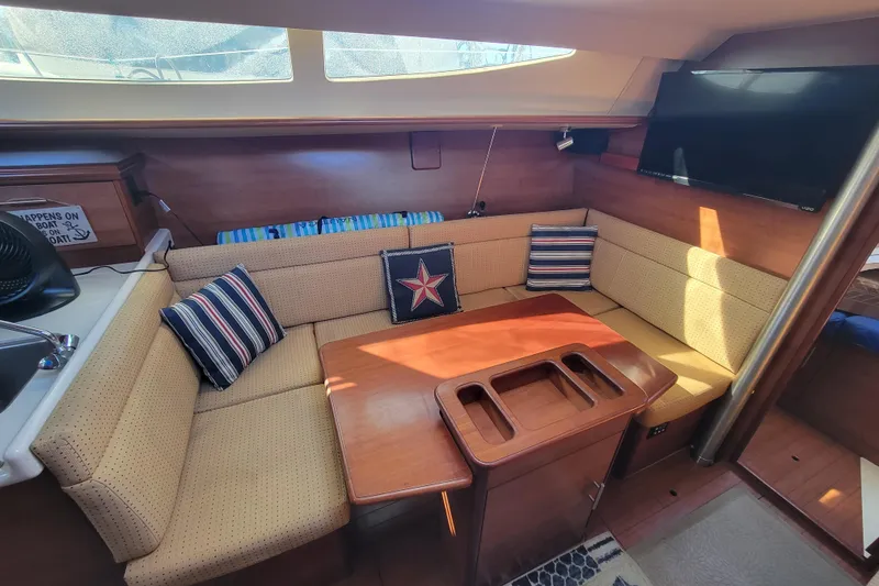 Slide: The Image of 2013 Hunter 33 yacht interior with cozy seating, striped cushions, and a mounted TV. - 5