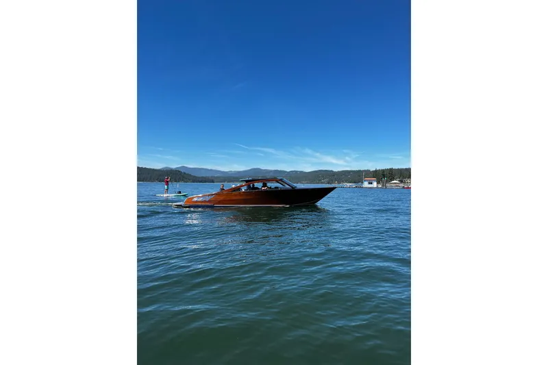 Slide: The Image of 2023 StanCraft 340 Darkside boat cruising on a serene lake under a clear blue sky. - 2