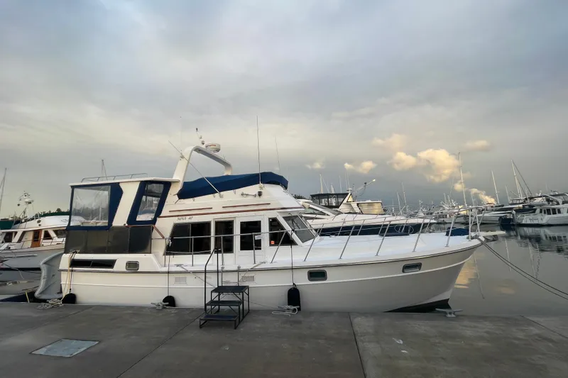 The Image of 1985 Nova 40 Sundeck Aft Cabin yacht docked at marina under cloudy sky. - 0