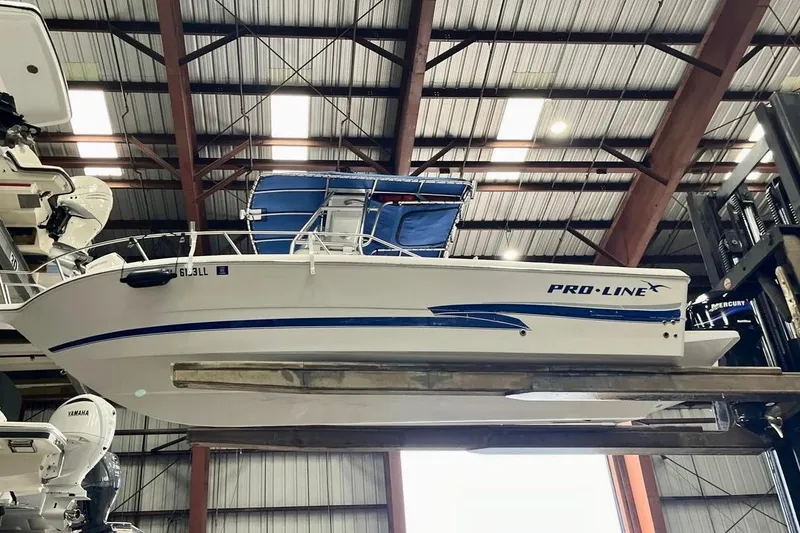 Slide: The Image of 2001 Pro-Line 25 Sport CC boat in storage, featuring blue accents and a covered top. - 0