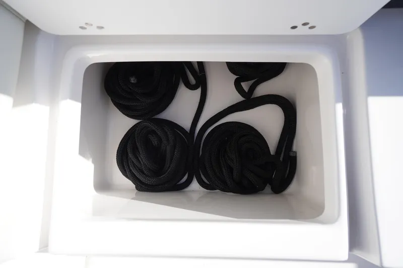 Slide: The Image of Storage compartment with coiled black ropes on a 2024 Tidewater 232 SS boat. - 10