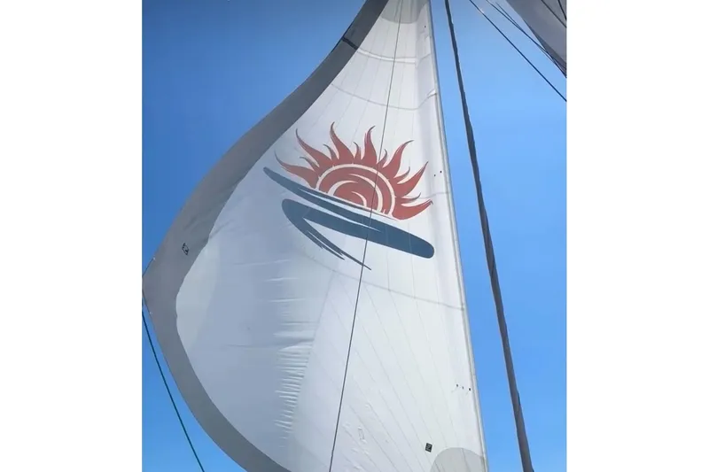 Slide: The Image of Sailboat with sun design on sail, Balance 482 model, 2023, against clear blue sky. - 132