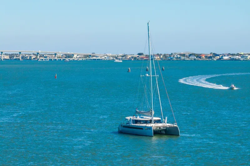 Slide: The Image of 2024 Balance 482 catamaran sailing on a calm blue sea near a coastal bridge. - 140