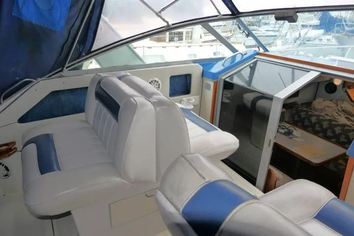 Slide: The Image of 1988 Sea Ray 300 Weekender interior with white and blue seating, cabin view, and marina backdrop. - 17