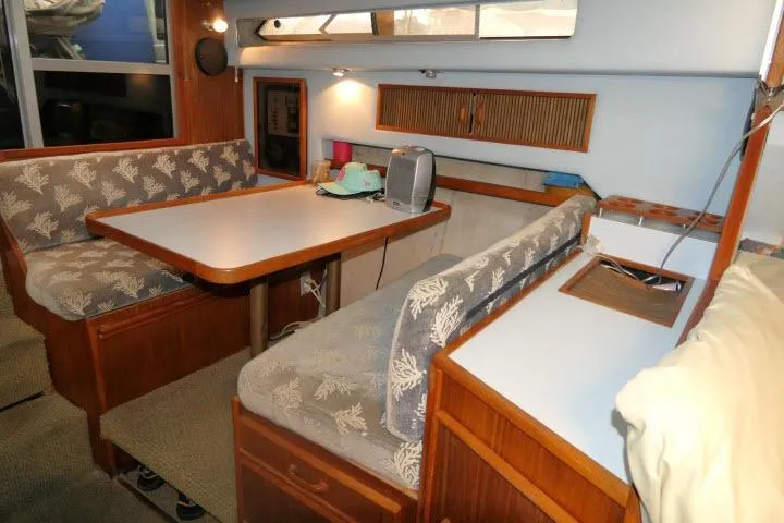 Slide: The Image of 1988 Sea Ray 300 Weekender interior with dining area, cushioned seating, and wooden cabinetry. - 5