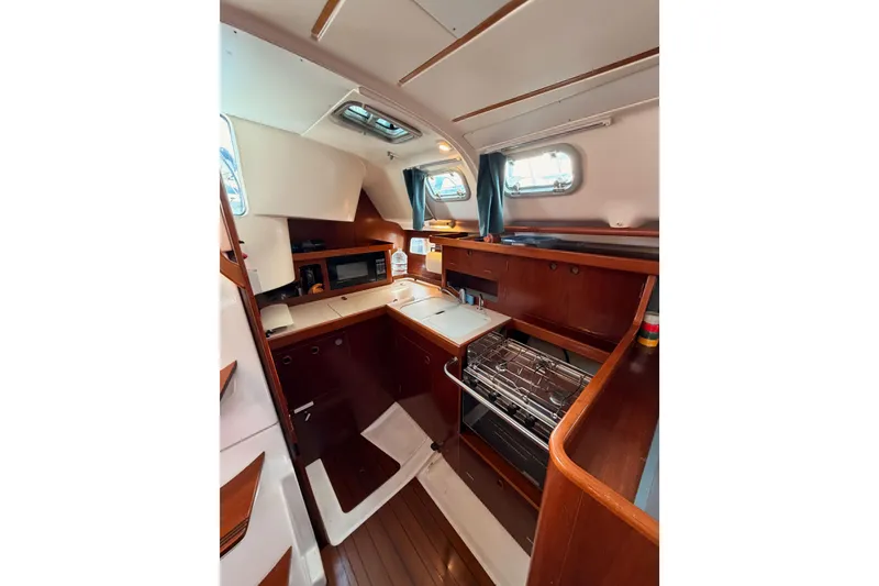 Slide: The Image of Interior of 1995 Beneteau Oceanis 351 sailboat, featuring a compact kitchen with wood finishes. - 35