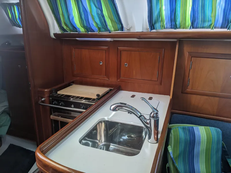 Slide: The Image of 2005 Beneteau 323 yacht interior with sink, stove, and colorful curtains. - 32