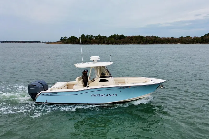 The Image of 2022 Grady-White Canyon 271 boat cruising on calm waters near a forested shoreline. - 0
