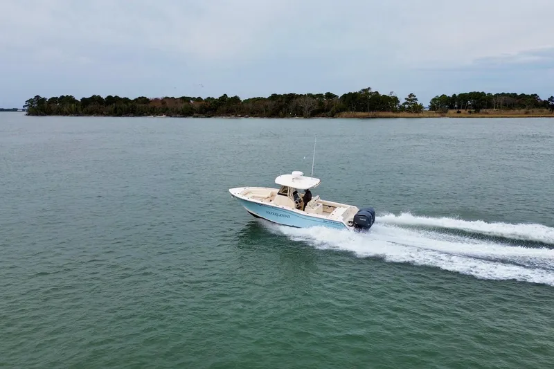 Slide: The Image of 2022 Grady-White Canyon 271 boat cruising on a calm lake near a forested shoreline. - 7