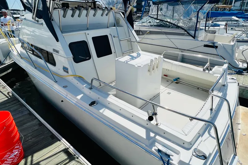 Slide: The Image of 2001 Skipjack 262 Flybridge boat docked, featuring spacious deck and fishing rod holders. - 1