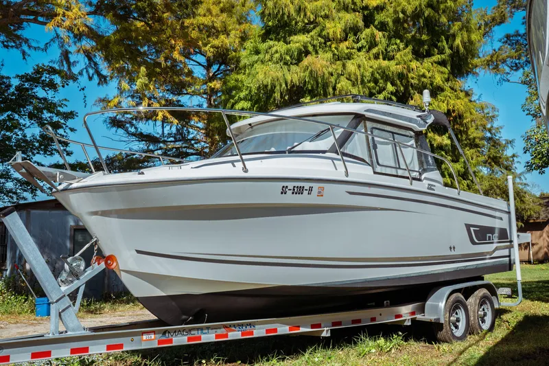 The Image of 2024 Jeanneau NC 795 Series 2 boat on trailer, surrounded by trees. - 0