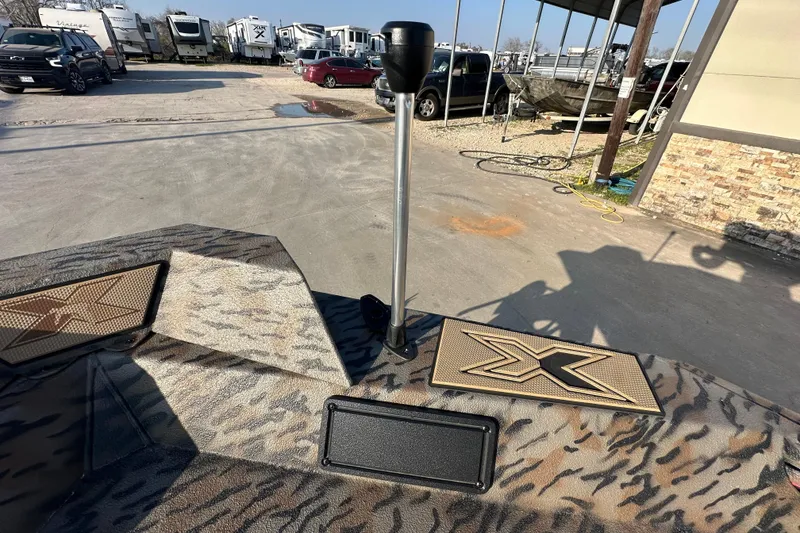 Slide: The Image of 2026 Xpress X18DB boat deck with camouflage pattern and logo, parked near RVs. - 20