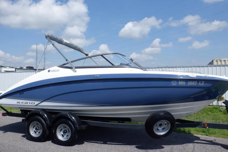 The Image of 2019 Yamaha SX210 boat on trailer, blue and white design, parked outdoors. - 0