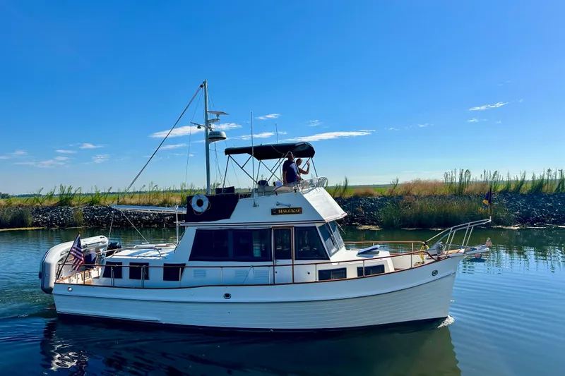 Slide: The Image of 1997 Grand Banks Classic yacht cruising on a serene river under a clear blue sky. - 6