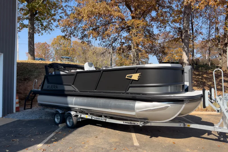 The Image of Alera M23Q 2026 pontoon boat on trailer, surrounded by autumn trees. - 1
