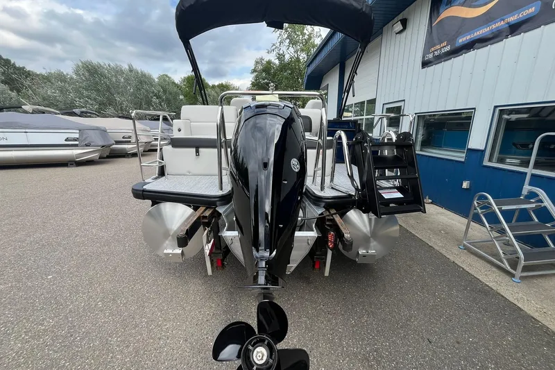 Slide: The Image of 2026 Harris Cruiser 210 pontoon boat with outboard motor, parked near a marine shop. - 3