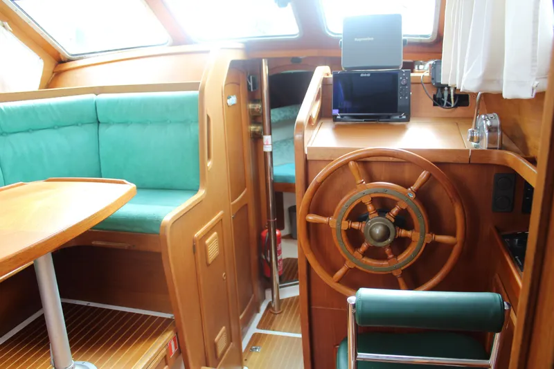 Slide: The Image of 1998 Nauticat 32 Pilothouse interior with wooden helm, green seating, and navigation equipment. - 10
