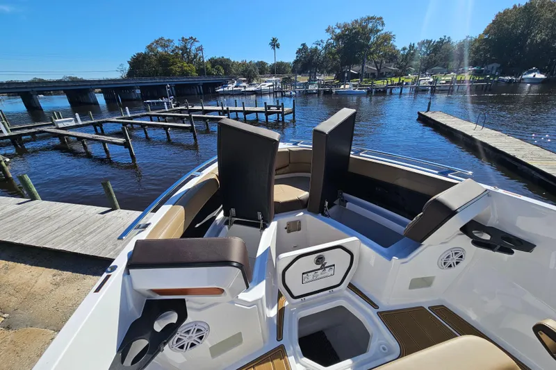 Slide: The Image of 2026 Monterey Elite 27 OB boat interior with seating, cup holders, and storage, docked by a scenic waterfront. - 36