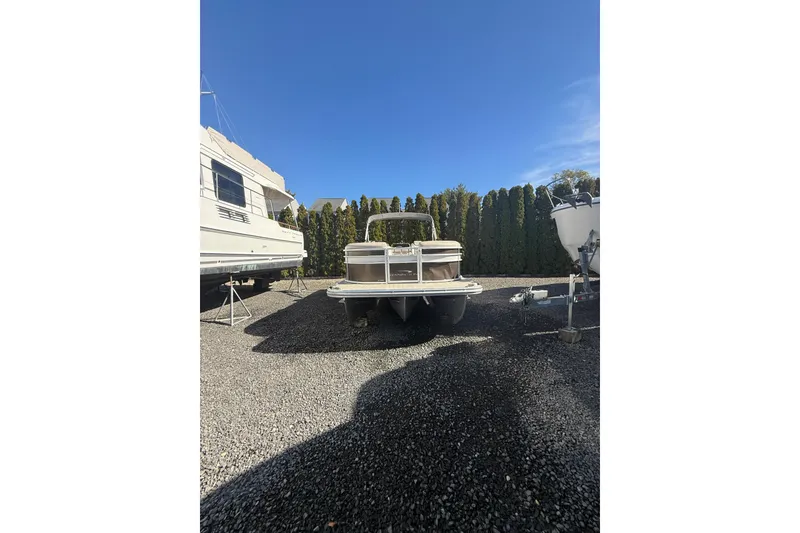 Slide: The Image of 2016 Bennington SX22 pontoon boat parked on gravel lot under clear blue sky. - 3