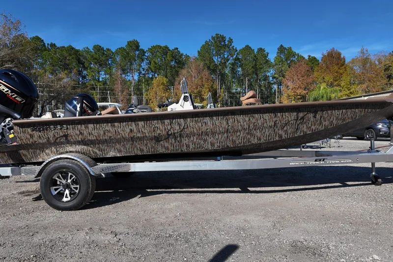 The Image of 2026 Xpress X18DB boat with camouflage design on a trailer, parked outdoors. - 0