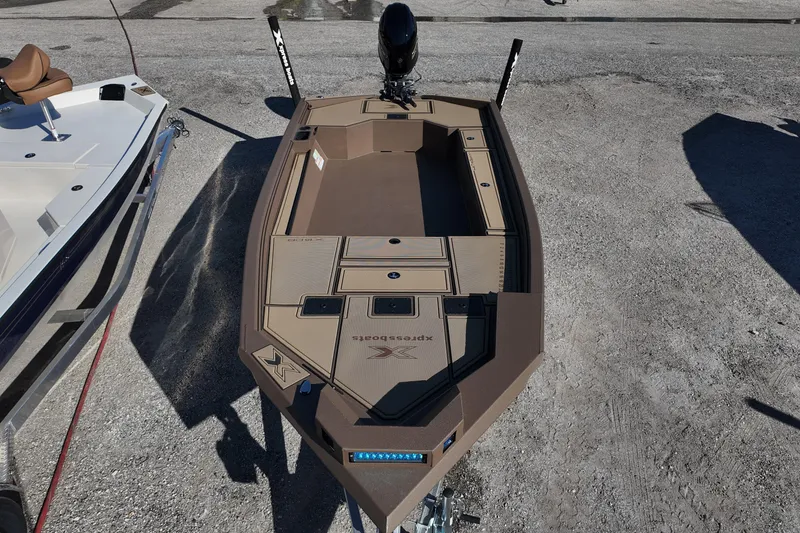 Slide: The Image of 2026 Xpress X18DB boat, brown deck, parked on gravel, with motor and accessories. - 8