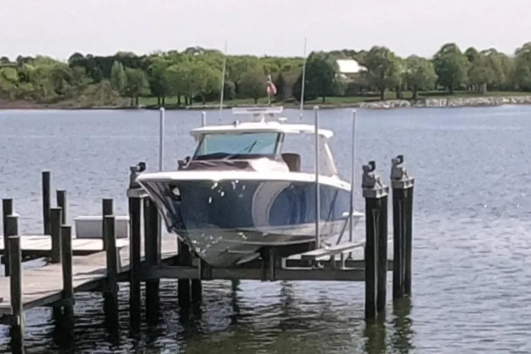 Slide: The Image of 2024 Tiara Yachts 43 LS docked on a lift by a serene lake. - 6