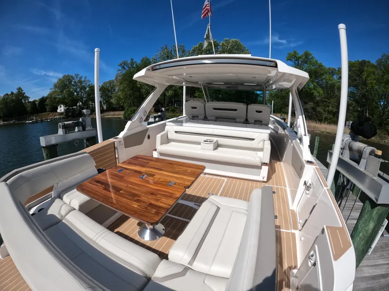 Slide: The Image of 2024 Tiara Yachts 43 LS with elegant seating and wooden table, docked by a serene waterfront. - 9