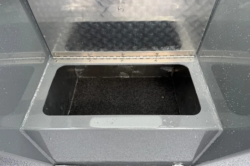 Slide: The Image of Open storage compartment in 2026 Fish Rite Sportsman 20 boat, featuring a metal lid and carpeted interior. - 21