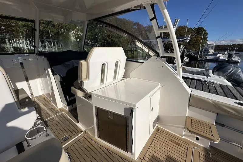 Slide: The Image of 2016 Pursuit DC 325 Dual Console boat interior with seating and storage, docked by the water. - 15