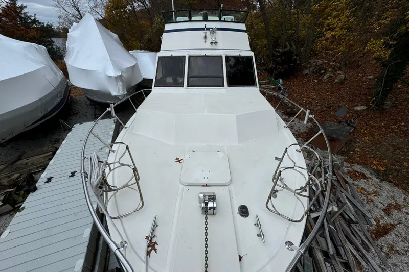 Slide: The Image of 1986 Stamas Flybridge Sedan boat on land, surrounded by autumn foliage and covered vessels. - 5