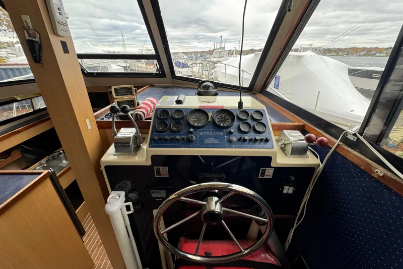 Slide: The Image of 1986 Stamas Flybridge Sedan helm with gauges, steering wheel, and marina view. - 8
