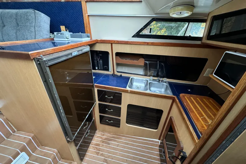 Slide: The Image of 1986 Stamas Flybridge Sedan interior with kitchen, featuring sink, fridge, and wooden cabinetry. - 9