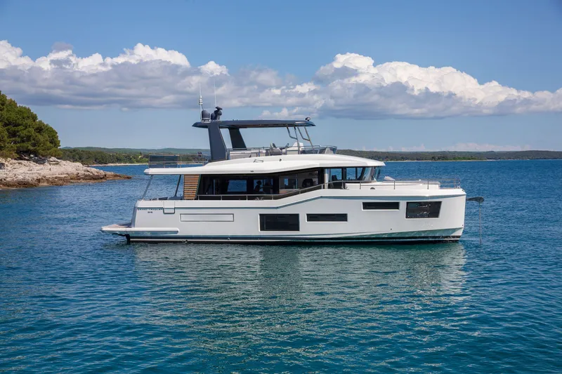 The Image of 2025 Beneteau Grand Trawler 63 yacht on serene blue waters under a clear sky. - 1