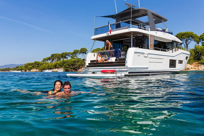 Slide: The Image of Couple swimming near 2025 Beneteau Grand Trawler 63 yacht in scenic coastal waters. - 24