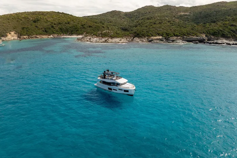 Slide: The Image of 2025 Beneteau Grand Trawler 63 cruising in clear blue waters near a lush coastline. - 36