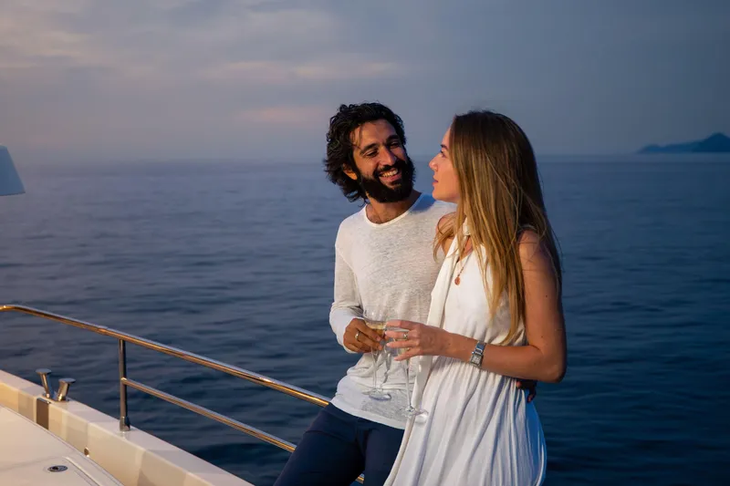 Slide: The Image of Couple enjoying sunset on 2025 Beneteau Grand Trawler 63 yacht, holding champagne glasses. - 44