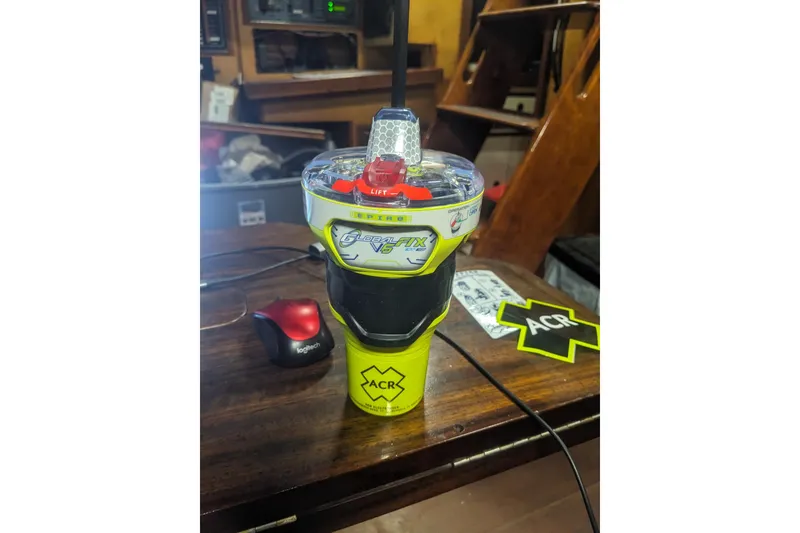 Slide: The Image of ACR GlobalFix V5 EPIRB on a wooden table, near a Logitech mouse. - 23