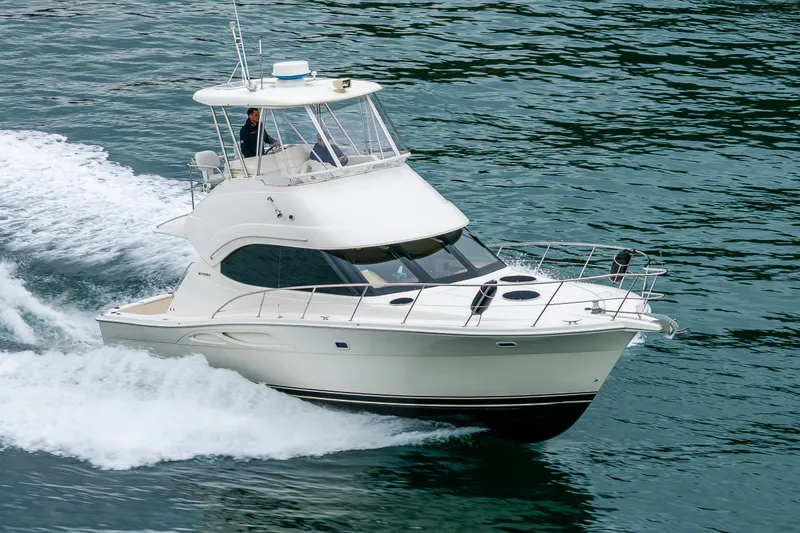 The Image of 2004 Riviera 37 Flybridge yacht cruising on scenic waters with forested islands. - 0