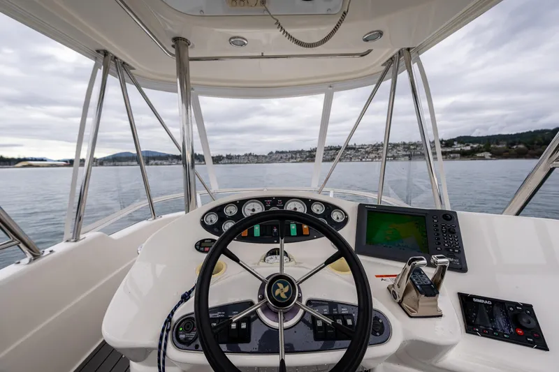 Slide: The Image of 2004 Riviera 37 Flybridge helm with navigation equipment, steering wheel, and scenic water view. - 23