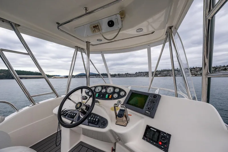 Slide: The Image of 2004 Riviera 37 Flybridge helm with navigation equipment, steering wheel, and scenic water view. - 24