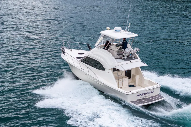 Slide: The Image of 2004 Riviera 37 Flybridge yacht cruising on open water with scenic island backdrop. - 6