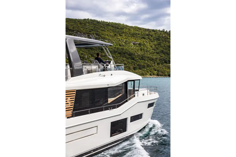 Slide: The Image of 2025 Beneteau Grand Trawler 63 cruising near lush green coastline. - 21