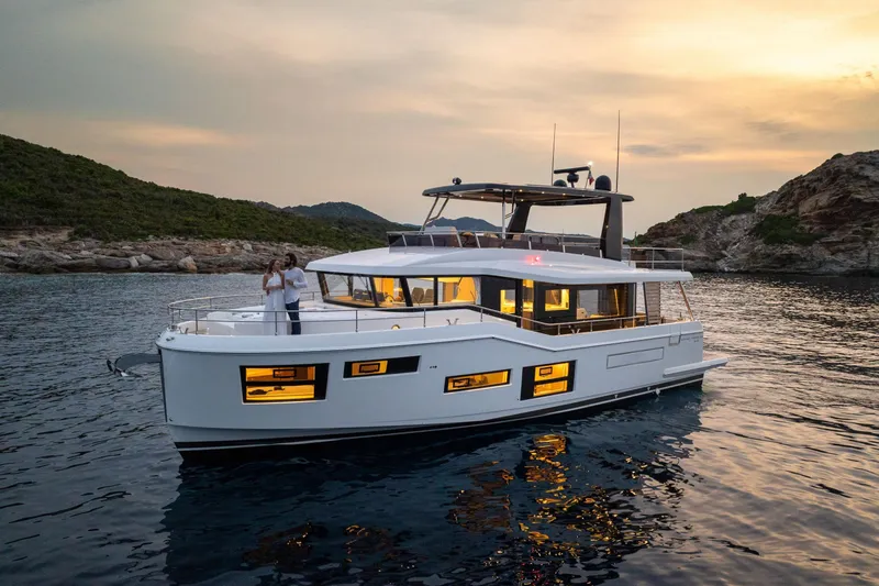 Slide: The Image of 2025 Beneteau Grand Trawler 63 yacht at sunset, anchored near rocky coastline. - 6