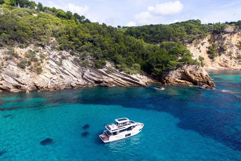 Slide: The Image of 2026 Beneteau Swift Trawler 54 cruising in clear turquoise waters near rocky coastline. - 33