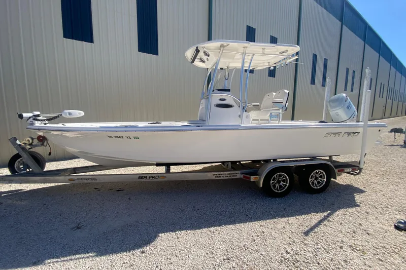 The Image of 2021 Sea Pro 248 Bay boat on trailer, parked outdoors near a large building. - 1