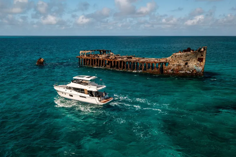 Slide: The Image of Beneteau Swift Trawler 48 (2026) cruising near a rusted shipwreck in clear blue waters. - 13